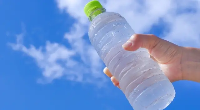 夏の青空にペットボトルをかざす