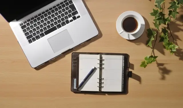 木目デスクに置かれたパソコンと手帳